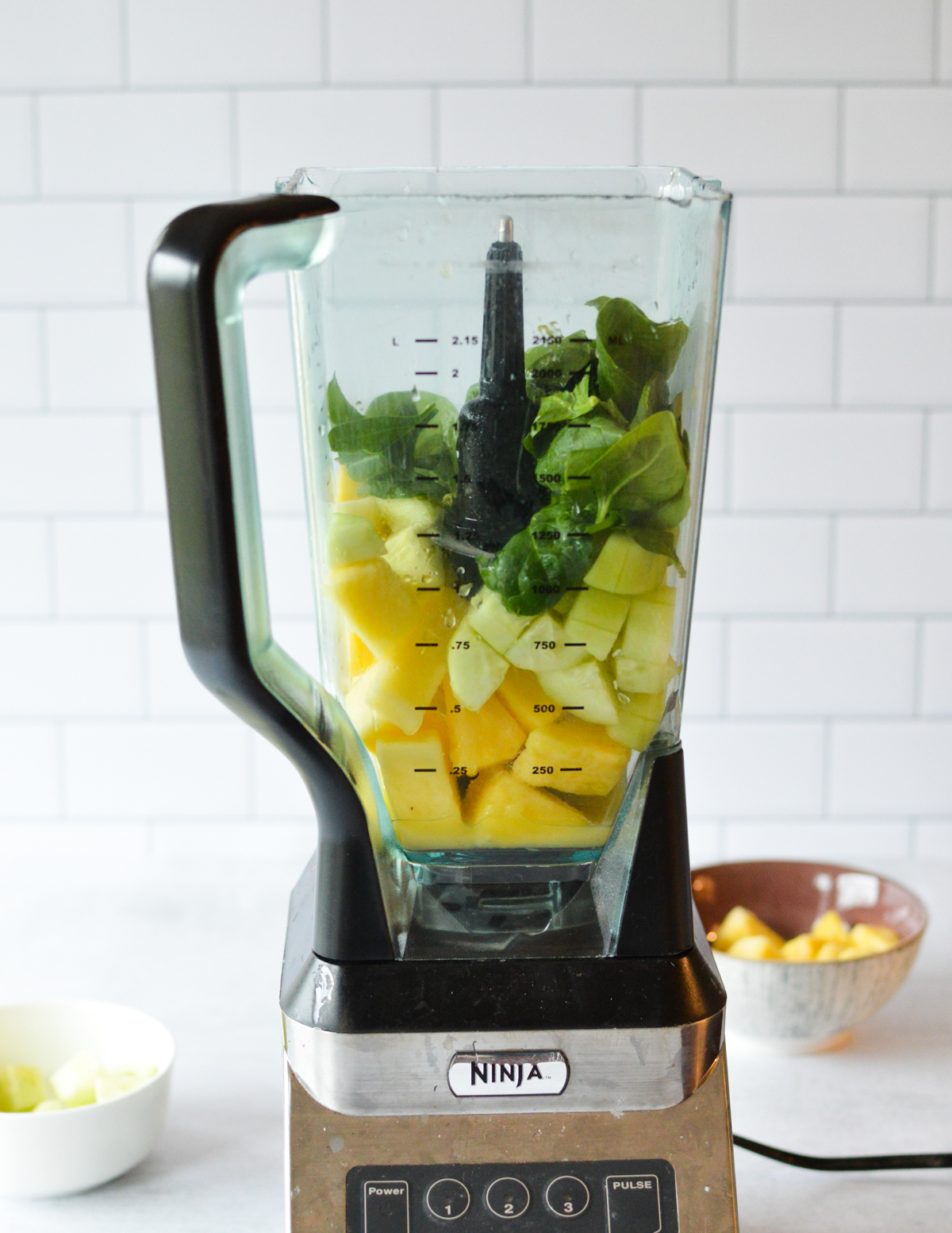 a blender with spinach, cucumber, and pineapple