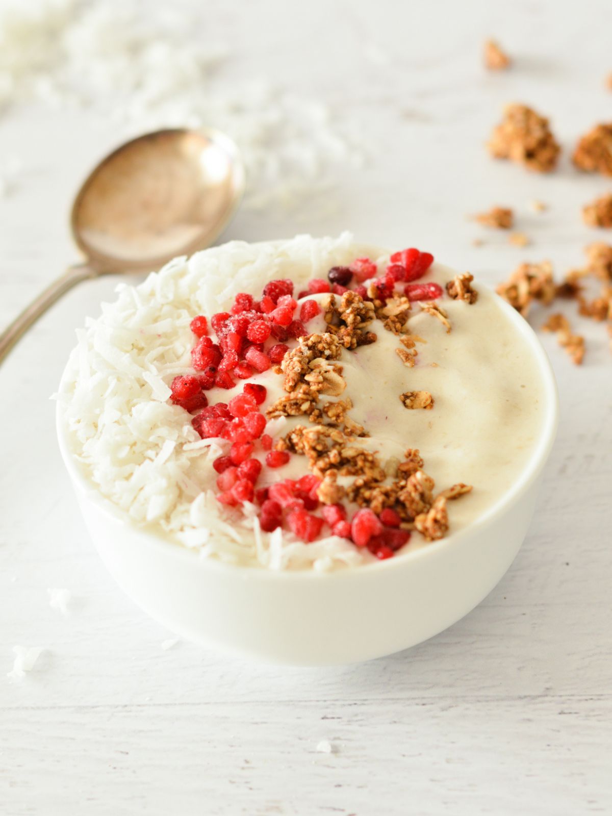 a coconut smoothie bowl with raspberries, coconut, and granola on top.