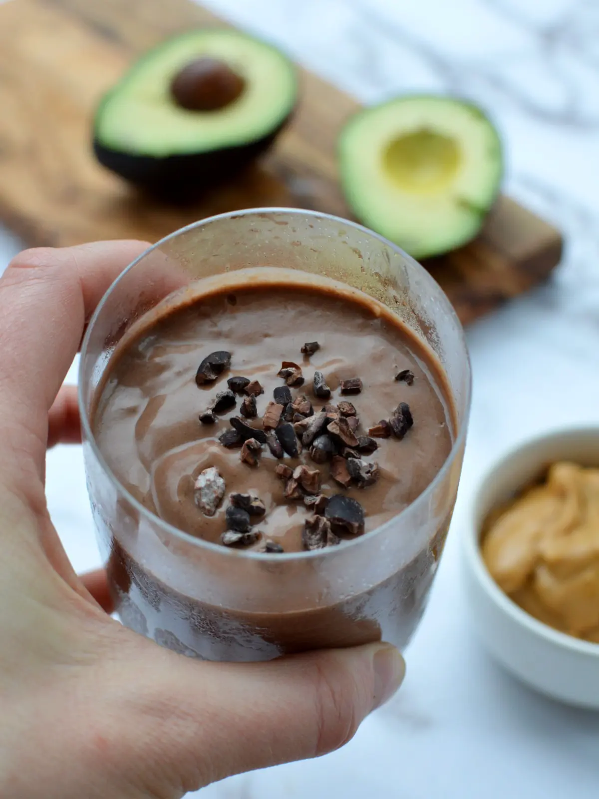 hand holding chocolate smoothie with cacao nibs on top. 