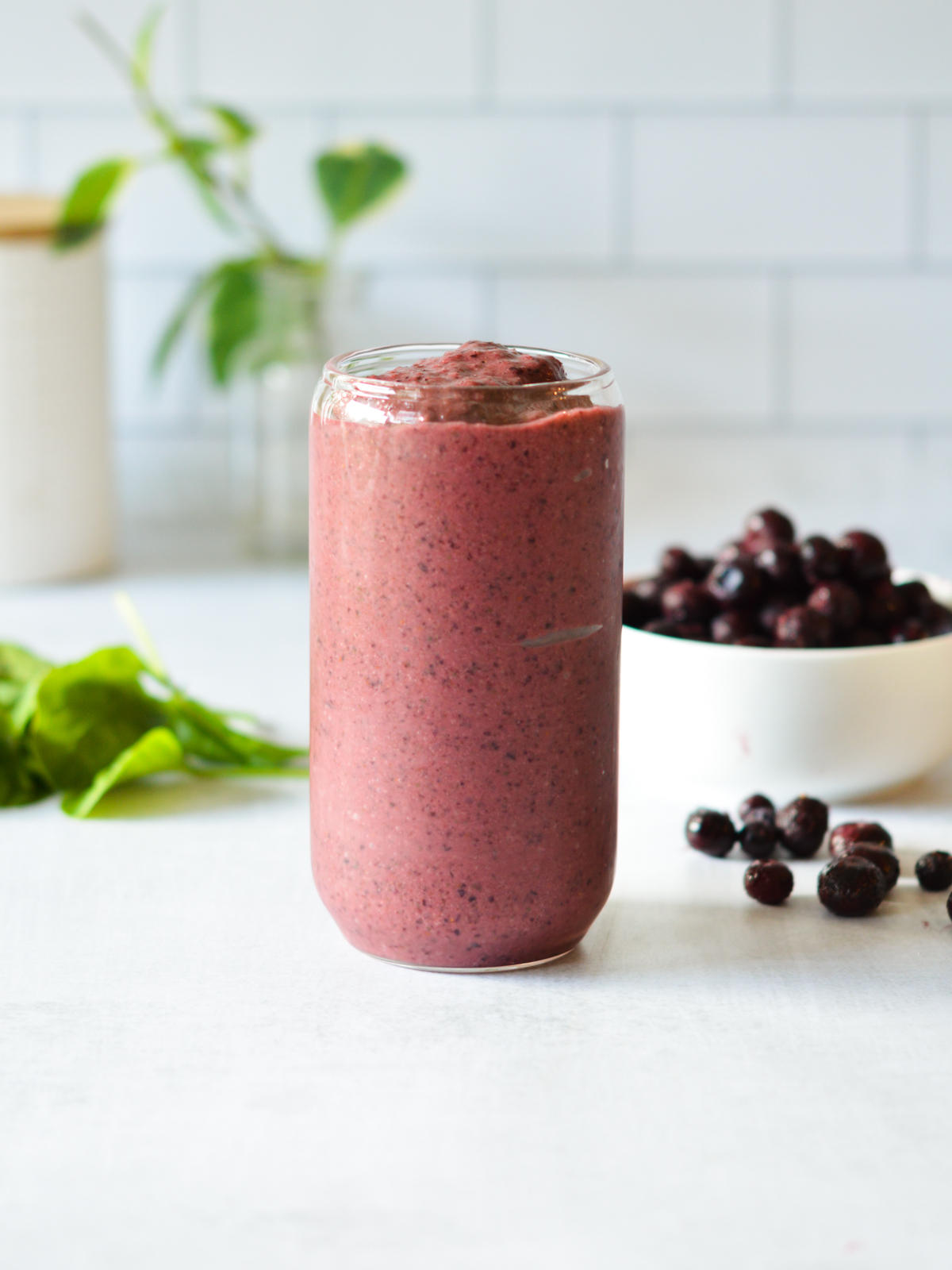 blueberry smoothie next to a bowl of blueberries and spinach.