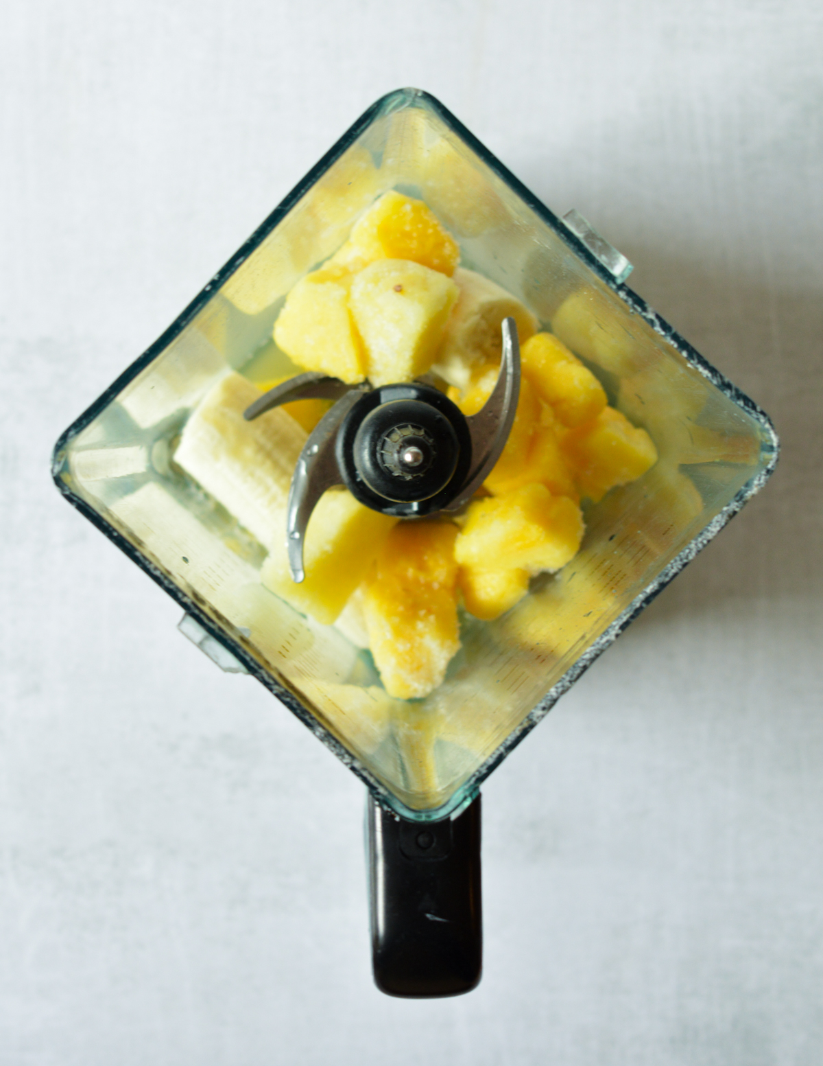 blender with pineapple, banana, and juice in it.