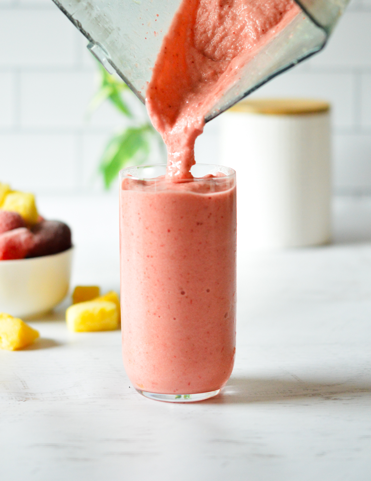 pouring a strawberry pineapple smoothie into a glass.