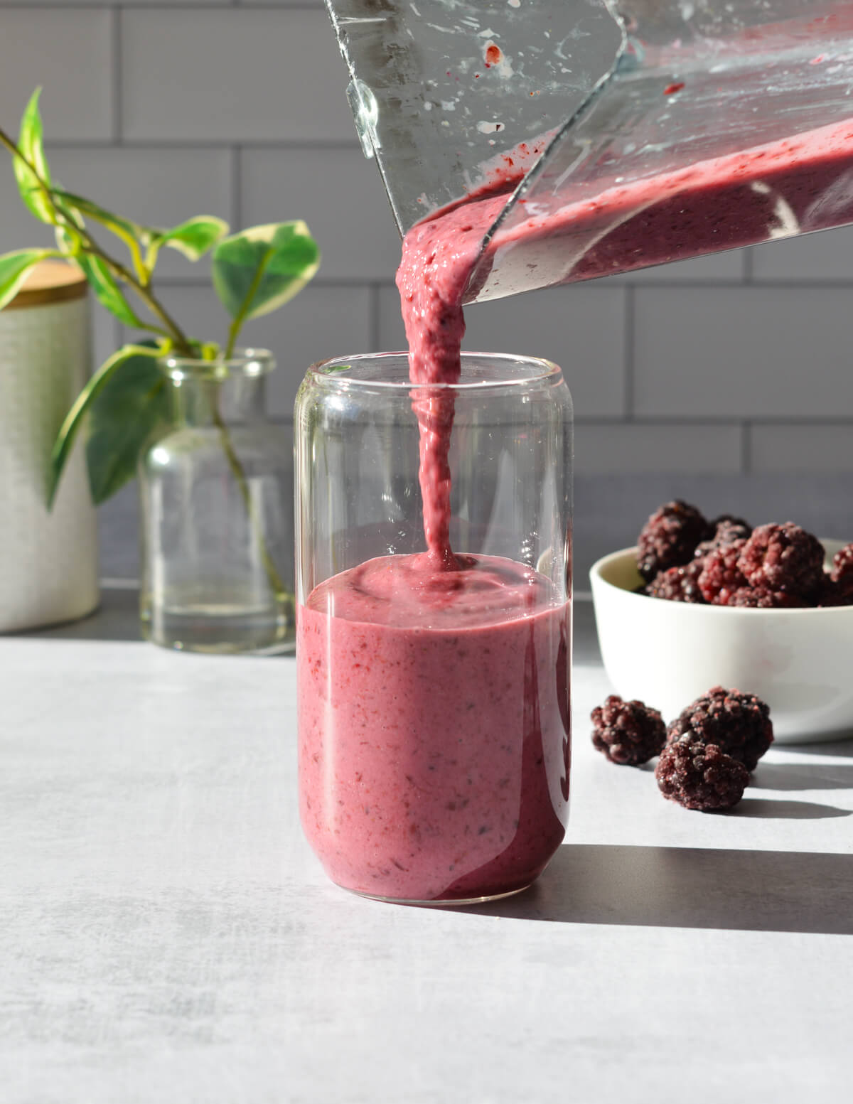 pouring a blackberry smoothie into a glass.