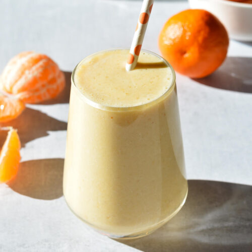 orange banana smoothie near some mandarin oranges.